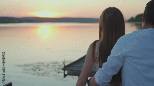 Young man and woman sitting together on a pier by the lake,