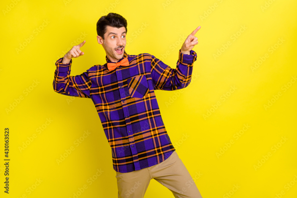 Photo of young handsome man happy smile look indicate finger empty space ad promo advice choice isolated over yellow color background Photo of young handsome man happy smile look indicate finger empty space ad promo advice choice isolated over yellow color background