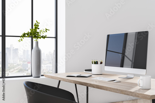 Sunny stylish room with cozy workspace  modern computer monitor on wooden table  city view from big window and light wall background