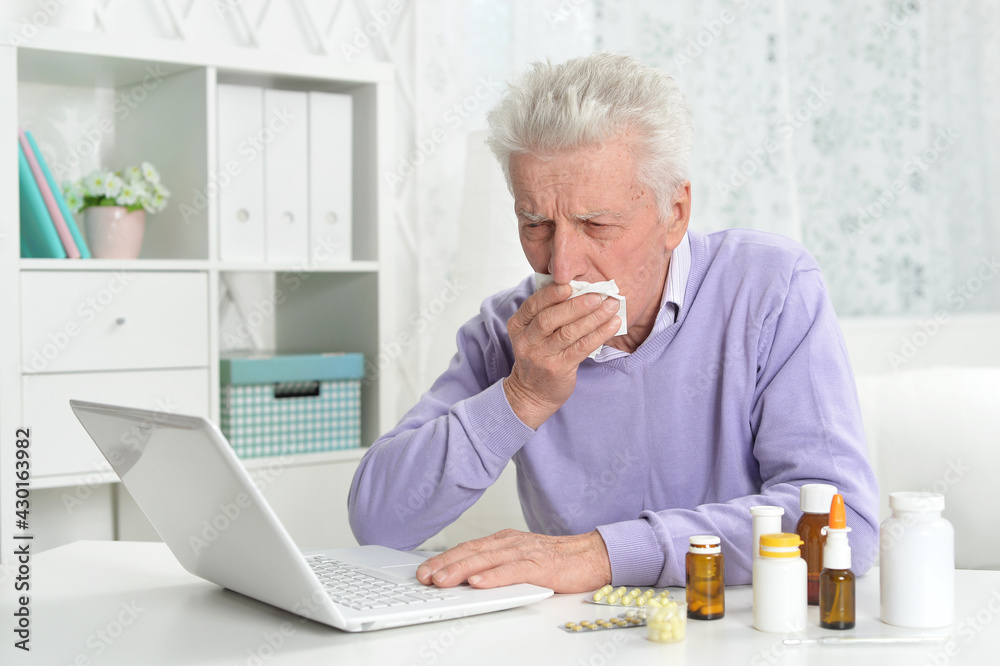 Fototapeta premium Portrait of sad sick senior man using laptop