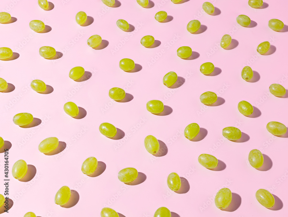 Pattern with fresh green grape berries against pastel pink background. Contemporary vegetarian fruit diet concept. Minimal summer food texture. Winery or vine store idea. Pattern with fresh green grape berries against pastel pink background. Contemporary vegetarian fruit diet concept. Minimal summer food texture. Winery or vine store idea.