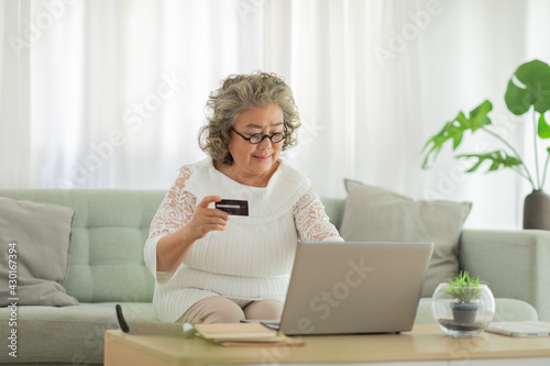 Happiness of wellness elderly asian woman with white hairs sitting on sofa using computer laptop and using credit card to shopping online and payment at home,Senior lifestyle at home concept