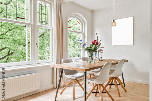 Table with flowers and chairs located near windows and abstract painting in light dining room at daytime