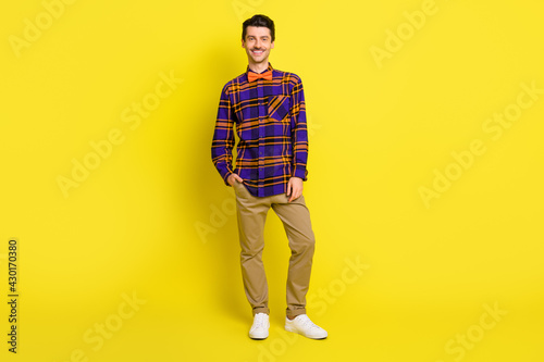 Photo of guy hand pocket beaming smile look camera wear bow tie plaid shirt isolated yellow color background