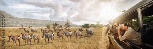 Group of young people watch and photograph wild zebras on safari tour in national park on Tanzania.