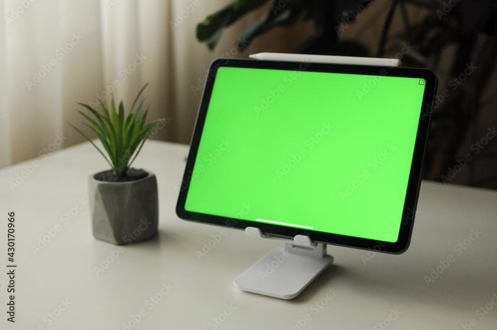 Tablet on stand with green background. Minimalism interior with homeplants Tablet on stand with green background. Minimalism interior with homeplants