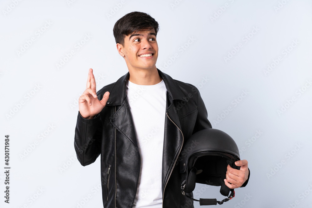 Man with a motorcycle helmet over isolated blue background with fingers crossing Man with a motorcycle helmet over isolated blue background with fingers crossing