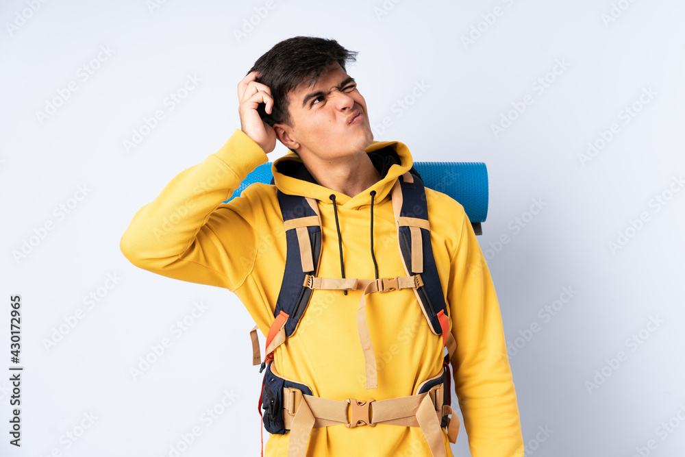 Young mountaineer man with a big backpack over isolated blue background having doubts and with confuse face expression Young mountaineer man with a big backpack over isolated blue background having doubts and with confuse face expression