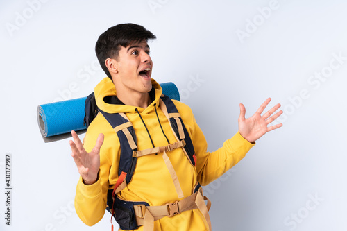 Young mountaineer man with a big backpack over isolated blue background with surprise facial expression