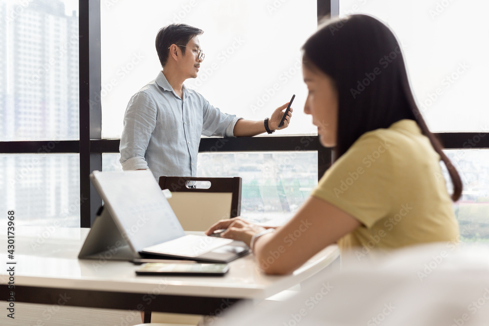 Businessman using cell phone with woman working on laptop in foreground. Businessman using cell phone with woman working on laptop in foreground.