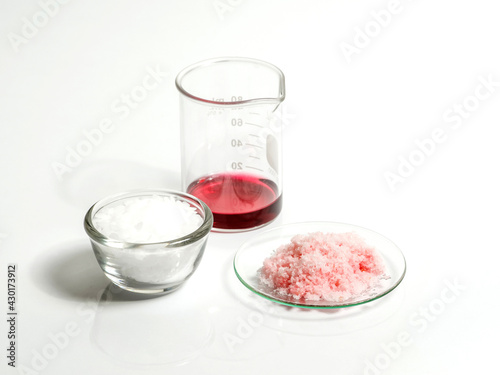Close up inorganic chemical on white laboratory table. Pink flake chemicals in Chemical Watch Glass, Red EPOXY liquid rasin in beaker, Microcrystalline wax in glass container.