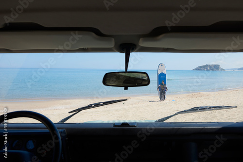 Paddle board and swimmer man on the beach looking at in the car.