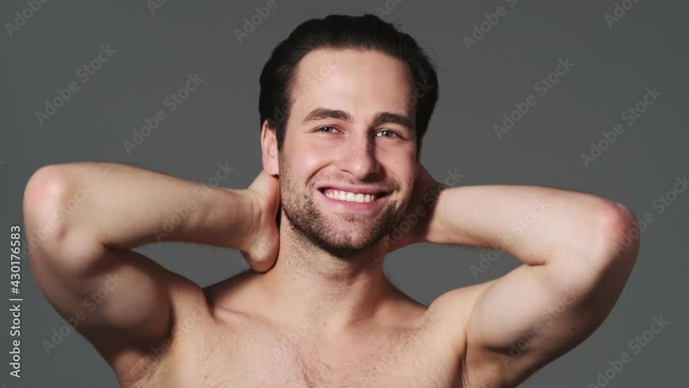A muscular man is posing to the camera standing isolated over grey wall in the studio A muscular man is posing to the camera standing isolated over grey wall in the studio