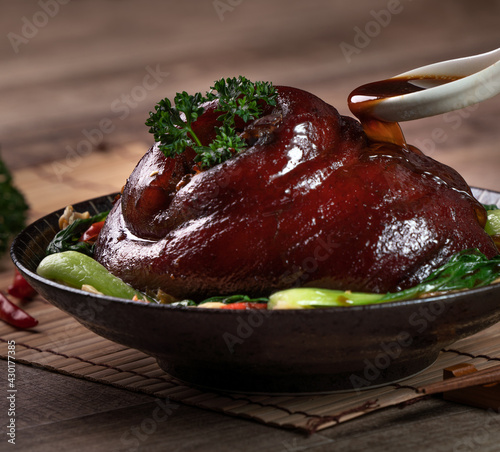 Pouring savory soy sauce with spoon over Taiwanese braised pork hock food in a plate. photo