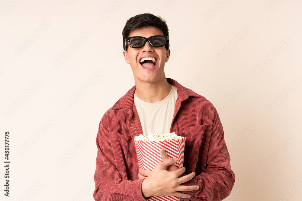 Handsome man over isolated background with 3d glasses and holding a big bucket of popcorns Handsome man over isolated background with 3d glasses and holding a big bucket of popcorns