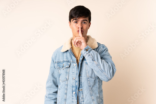 Handsome man over isolated beige background showing a sign of silence gesture putting finger in mouth