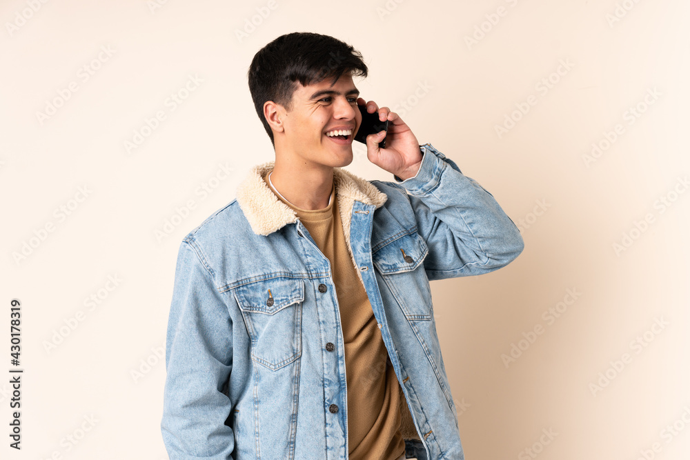 Handsome man over isolated beige background keeping a conversation with the mobile phone Handsome man over isolated beige background keeping a conversation with the mobile phone