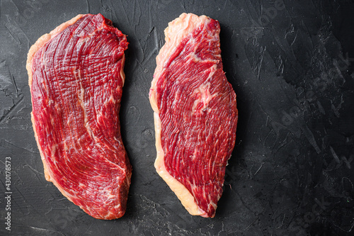 Set of picanha raw beef steaks on black textured background, top view space for text.