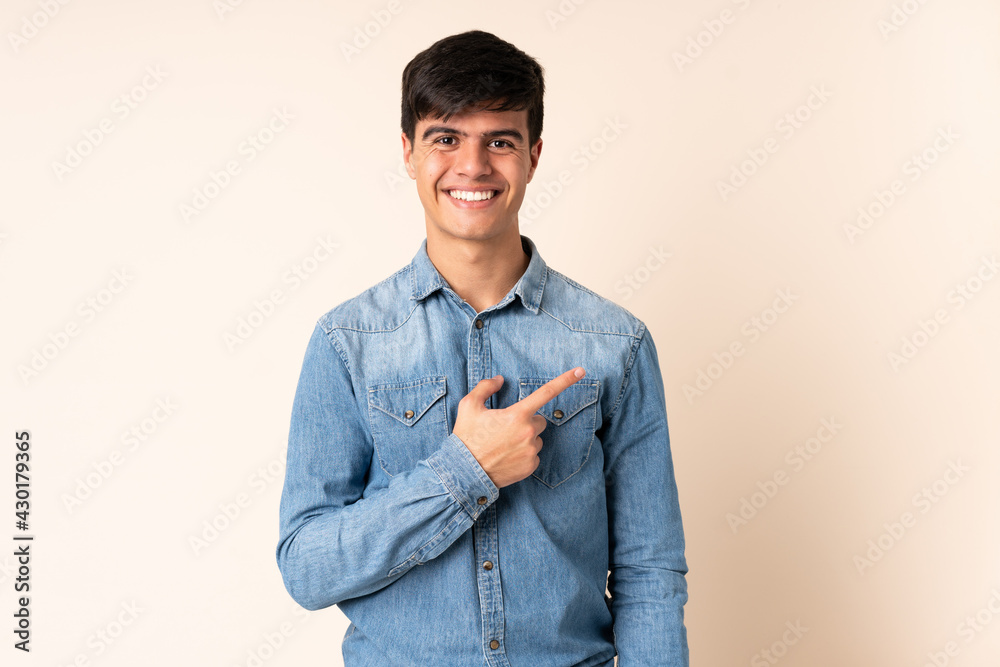 Handsome man over isolated beige background pointing to the side to present a product Handsome man over isolated beige background pointing to the side to present a product
