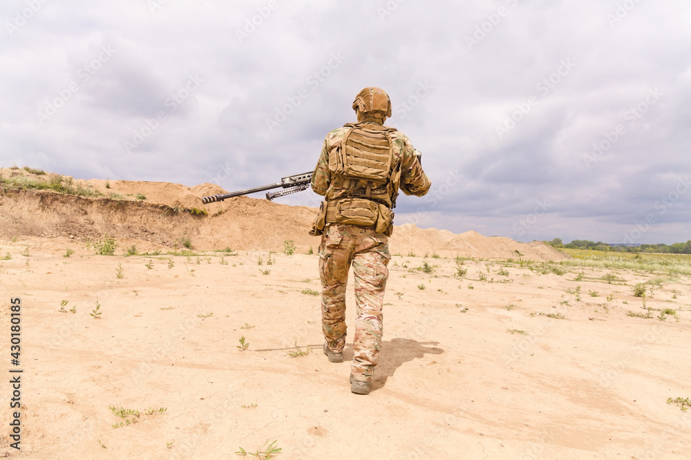 Special force soldier in camouflage with rifle walks across desert