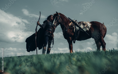 Fotografie Woman in image of medieval warrior stands near horse in field.