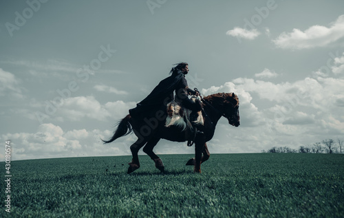 Fotografie Woman in image of medieval warrior rides on galloping horse.