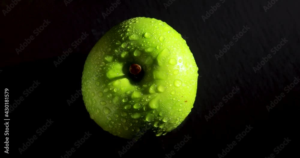 A green apple rotating on a black background, top view. High quality 4k footage