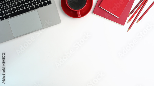 Top view office desk with laptop computer, red cup coffee, red notebook and pencil on white table.