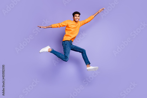 Full body photo of brunette afro american man wear jeans go empty space jump isolated on violet color background