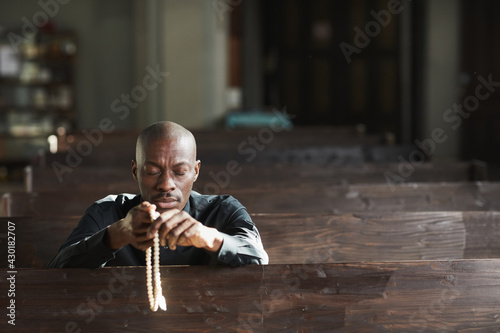 Fototapeta Naklejka Na Ścianę i Meble -  African man sitting in the church holding beads and praying with his eyes closed