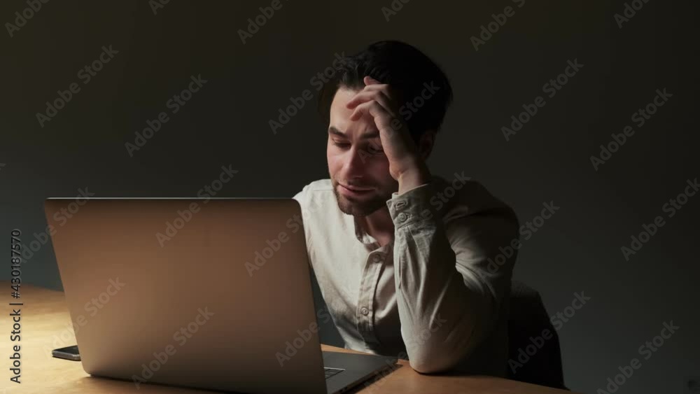 A serious focused man is working his laptop computer while sitting at the table at night time A serious focused man is working his laptop computer while sitting at the table at night time