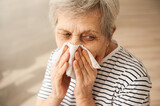 An elderly woman blows her nose.