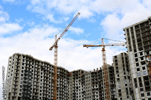 Construction cranes above unfinished residential buildings on blue sky and white clouds background. Housing construction, apartment block in city
