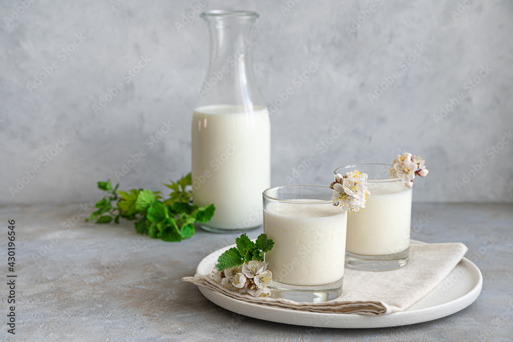Fresh homemade milk drink-yogurt, kefir, ayran, lassi, in two glasses on a gray background with greenery and flowers. Fresh homemade milk drink-yogurt, kefir, ayran, lassi, in two glasses on a gray background with greenery and flowers.