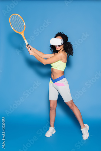 full length of curly african american woman in vr headset playing tennis on blue © LIGHTFIELD STUDIOS
