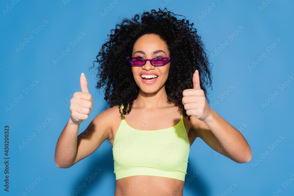 happy african american woman in sunglasses showing thumbs up on blue happy african american woman in sunglasses showing thumbs up on blue