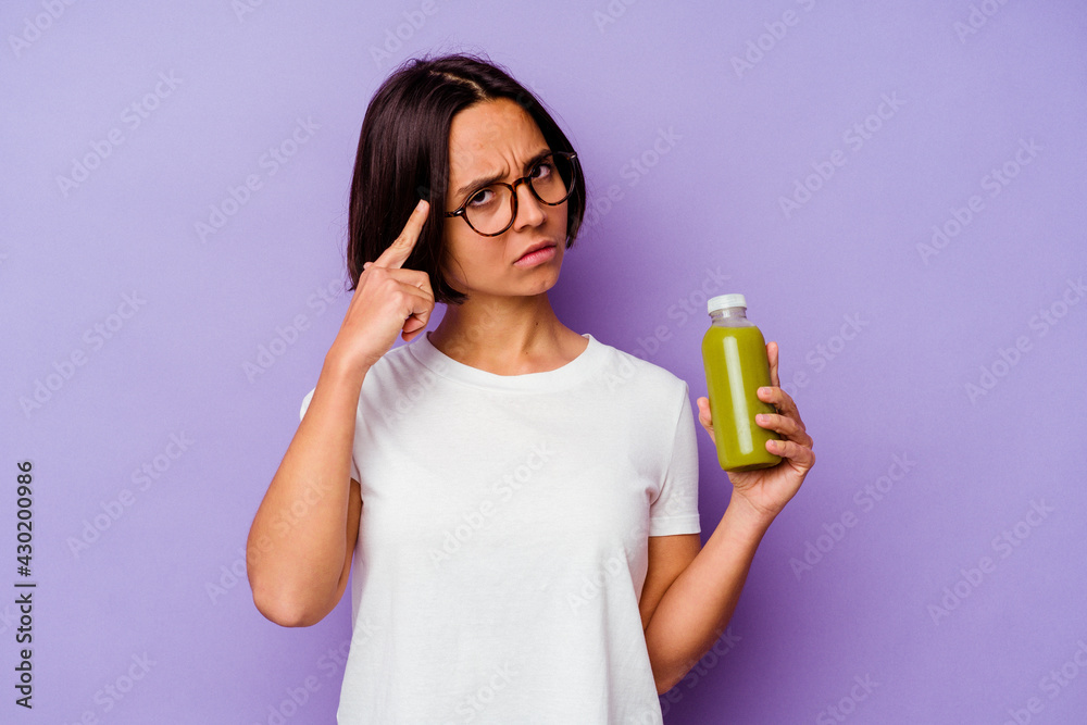 Young mixed race woman holding a healthy smoothie isolated on purple background pointing temple with finger, thinking, focused on a task. Young mixed race woman holding a healthy smoothie isolated on purple background pointing temple with finger, thinking, focused on a task.