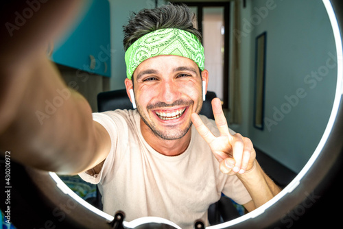 Happy hispanic millennial man making video call at home - Young guy taking a selfie smiling at camera indoor - People, vlog, influencers and dating online concept photo