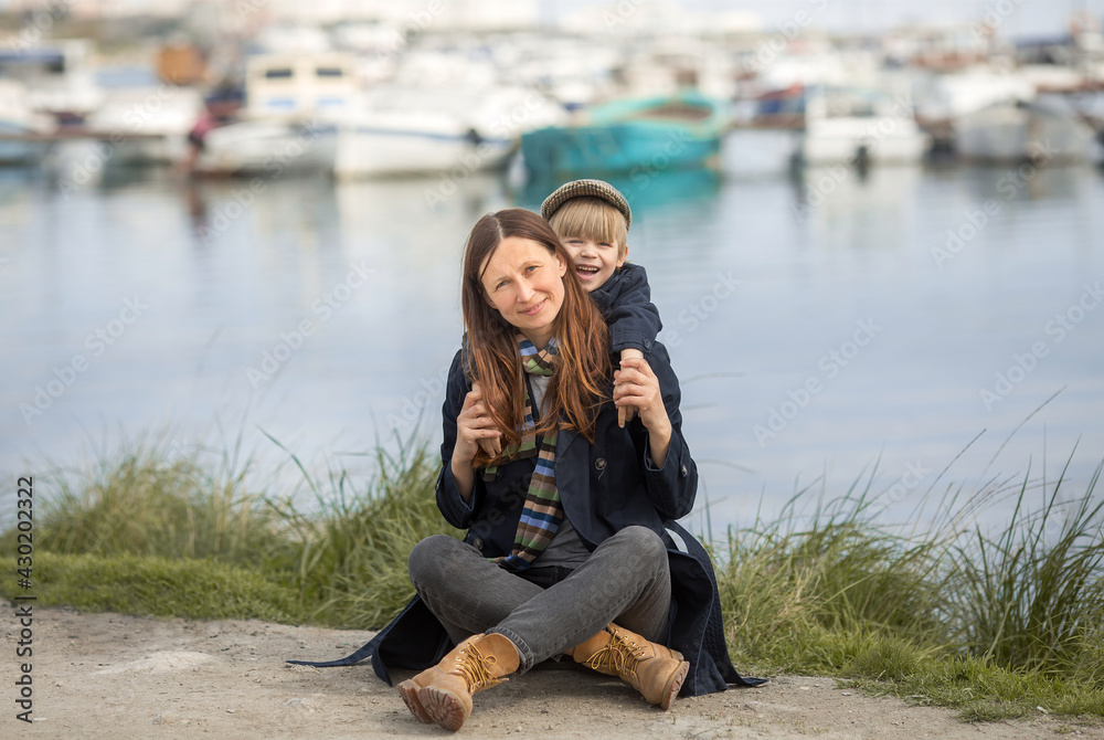 a woman and her child are playing in the seashore, the son is hanging on the neck of the mother, they are laughing. the concept of mother's love for her son