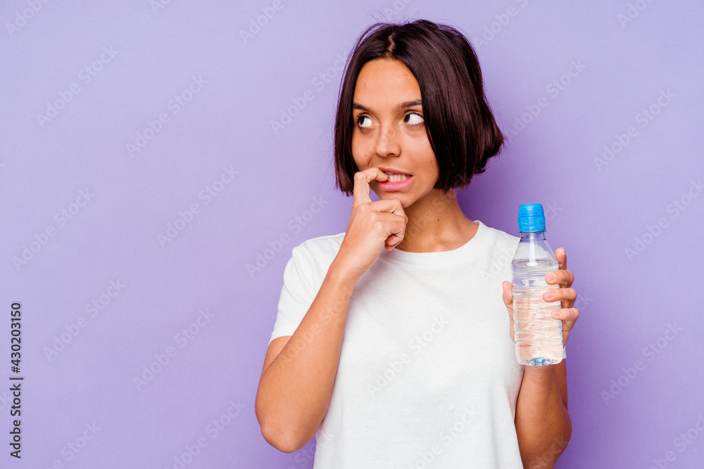 Young mixed race holding a water bottle isolated on purple background relaxed thinking about something looking at a copy space. Young mixed race holding a water bottle isolated on purple background relaxed thinking about something looking at a copy space.