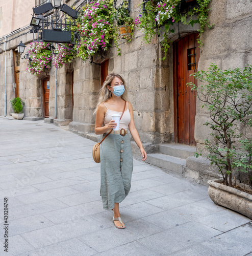 Woman wearing protective face mask with mobile phone video calling friends outdoors city street