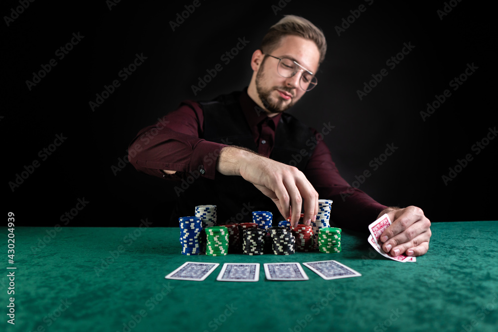 Young handsome poker player sitting at a green gaming table with a lot of chips and good cards.