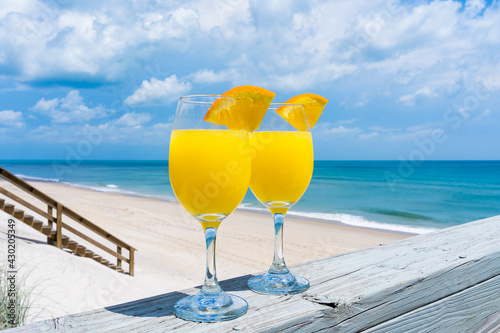 Bright yellow glasses of mimosa cocktails in the bright sun on the railing of the veranda of a private house by the ocean for brunch