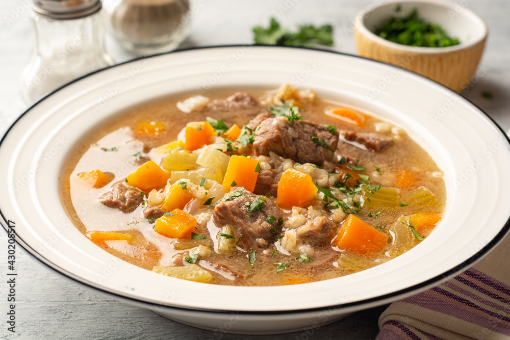 Beef and barley soup with celery, carrot and onion in plate on concrete background Beef and barley soup with celery, carrot and onion in plate on concrete background