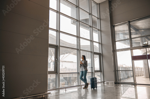 Caucasian woman is standing alone near airport terminal panoramic windows with luggage © Yaroslav Astakhov