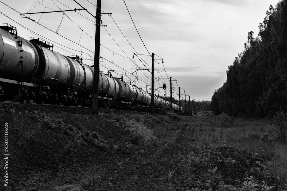 Obraz premium railway black-white landscape. the freight train goes far. transportation of goods and fuel tanks by rail. black and white photo of a freight train