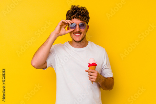 Young caucasian man eating an ice cream isolated on yellow background excited keeping ok gesture on eye.