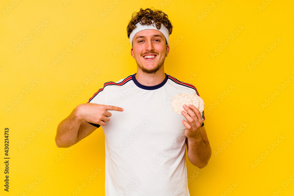 Young sport caucasian man eating a rice cake isolated on yellow background person pointing by hand to a shirt copy space, proud and confident Young sport caucasian man eating a rice cake isolated on yellow background person pointing by hand to a shirt copy space, proud and confident