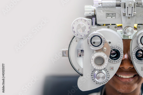 Close-up Of african teen girl Doing Eye Test On Phoropter, African teen girl checking on her eye with optometry machine. copy space background for text photo