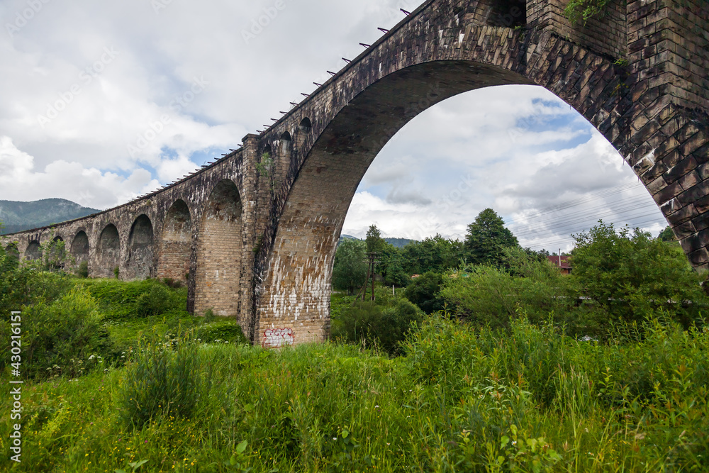 Old bridge viaduct in the mountains in summer among green grass and trees.